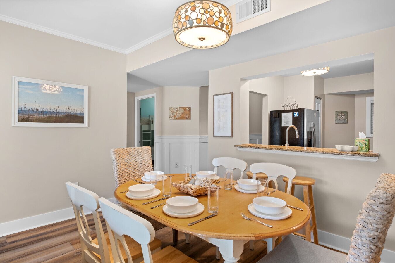 A dining area with a wooden table set for four, white chairs, and a hanging light fixture.