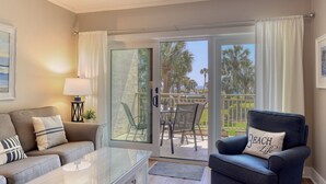 A living room with a sofa, armchair, and a glass coffee table. - MyStay at 136 Shorewood | Ocean + Pool Views | Walk to Coligny | Sleeps 6 (Hilton Head Island)