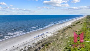 A coastal beach with a clear sky, a sandy shore, and a path leading to beach umbrellas. - MyStay at 136 Shorewood | Ocean + Pool Views | Walk to Coligny | Sleeps 6 (Hilton Head Island)