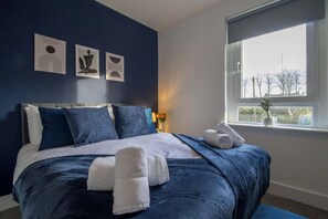 A bedroom with a bed, pillows, a window, and wall art. - The Wishy - 2 Bedroom Flat in Newmains (Newmains)