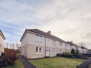 A two-story residential building with a flat roof, a front door, and a small front yard. - The Wishy - 2 Bedroom Flat in Newmains (Newmains)