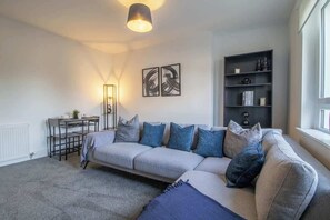 A modern living room with a sofa, a coffee table, a bookshelf, and a pendant light. - The Wishy - 2 Bedroom Flat in Newmains (Newmains)