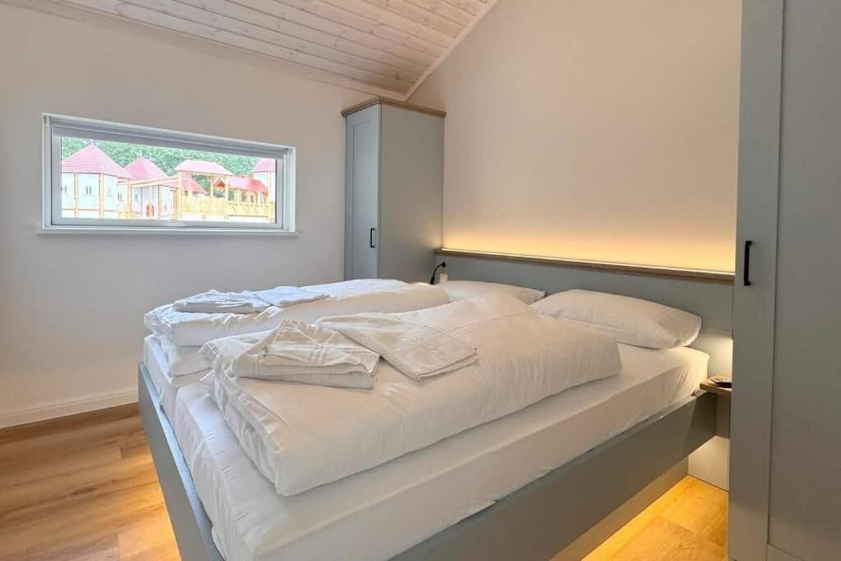 Une chambre avec un lit, une fenêtre donnant sur des maisons et un plafond en bois.