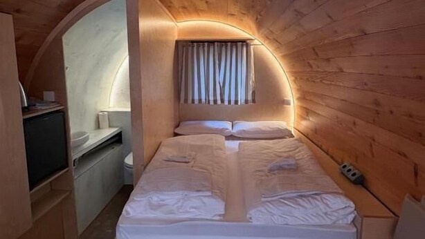 Une petite pièce avec un plafond voûté, un lit, un petit bureau et des toilettes.