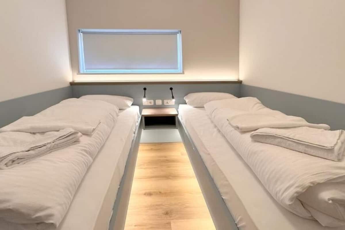 Une chambre avec deux lits, un plancher en bois, un luminaire fixé au mur et une fenêtre donnant sur un beau paysage.