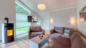 Un salon moderne doté d’un poêle à bois, de canapés en cuir, d’une table basse et d’une grande fenêtre offrant une vue sur la verdure.