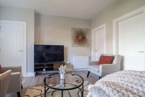 A living room with a flat-screen TV, a round coffee table, a sofa, and a decorative wall piece. - Sleeps 5 with walk in Shower, Rutherglen - Glasgow (Rutherglen)