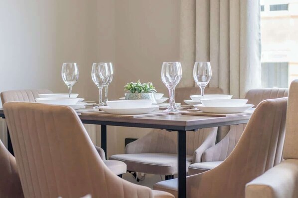 A dining table set with white plates and glasses, a small potted plant, and beige upholstered chairs. - Sleeps 5 with walk in Shower, Rutherglen - Glasgow (Rutherglen)