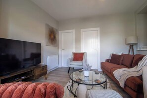 A modern living room with a flat-screen TV, a glass coffee table, a sofa, and a chair.