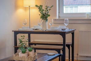 A dining table set with white plates, glasses, and a vase with green foliage. - Raeburn House- 3 Bedrooms, 2 Bathrooms in Hamilton (Hamilton)