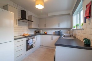 A modern kitchen with white cabinets, a built-in oven, a microwave, and a kettle. - Raeburn House- 3 Bedrooms, 2 Bathrooms in Hamilton (Hamilton)