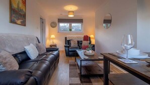 A living room with a sofa, a dining table with a wine glass, a window with a view, and a painting on the wall. - Raeburn House- 3 Bedrooms, 2 Bathrooms in Hamilton (Hamilton)