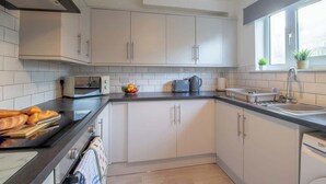 A modern kitchen with white cabinets, a black countertop, a built-in oven, and a window with plants. - Raeburn House- 3 Bedrooms, 2 Bathrooms in Hamilton (Hamilton)
