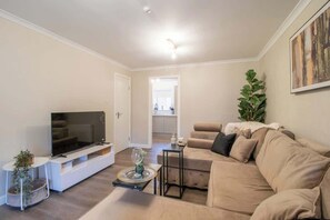 Ein Wohnzimmer mit Fernseher, Sofa und einem kleinen Tisch mit einem Glas.