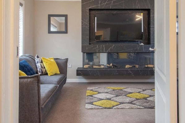 A living room with a sofa, a fireplace, and a television mounted on a marble wall.