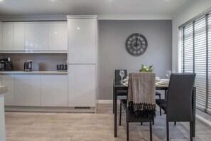 A modern kitchen with white cabinets, a clock on the wall, and a dining area with a table and chairs.