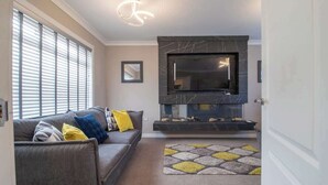 A living room with a sofa, a flat-screen TV, a fireplace, and a patterned rug. - Catriona House - 3 Bedroom house in Motherwell (Holytown)
