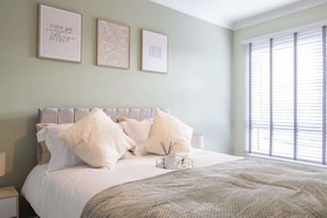 A bedroom with a bed, pillows, a bedside table, and wall art.