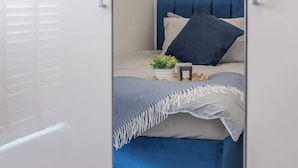 A bedroom with a bed, pillows, a small plant, and a bedside table. - Catriona House - 3 Bedroom house in Motherwell (Holytown)