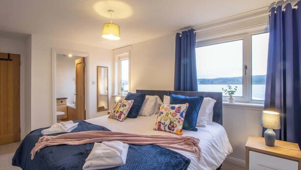 Una camera da letto con un letto, un comodino con una lampada, una finestra con tende e vista sull'esterno.