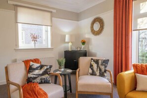 A room with two armchairs, a small table, a cabinet, a window with a view, and a decorative mirror on the wall. - The Bridge- 3 Bedrooms in Coatbridge with Driveway (Coatbridge)