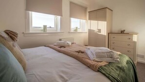 A bedroom with a bed, two windows with blinds, a dresser, and a radiator.