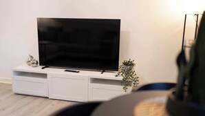 Una sala de estar moderna con un televisor de pantalla plana sobre un mueble blanco, una planta pequeña y una silla negra.