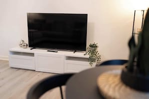 A modern living room with a flat-screen TV on a white entertainment unit, a small plant, and a black chair. - The Green- 2 Bed Flat near Aberdeen Ferry Terminal (Aberdeen)