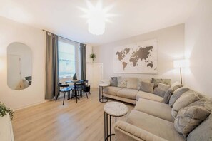 A modern living room with a sofa, a round coffee table, a dining area with chairs, a world map on the wall, and a large window. - The Green- 2 Bed Flat near Aberdeen Ferry Terminal (Aberdeen)