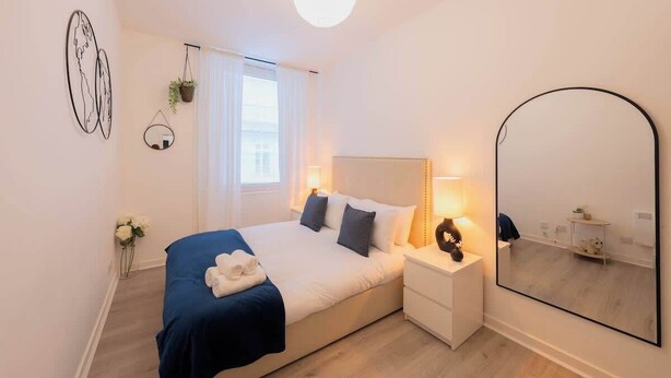 Un dormitorio con cama, mesita de noche, lámpara, espejo y decoración en la pared.