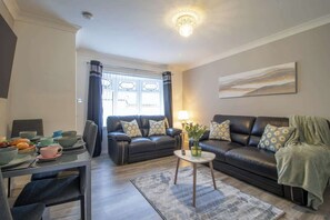 A living room with a sofa, a coffee table, a dining table with chairs, and a window with curtains. - Culzean House - 2 Bedrooms in Coatbridge (Coatbridge)
