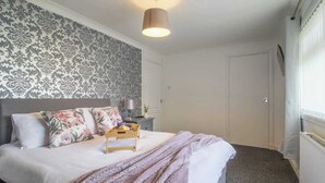 Ein Schlafzimmer mit Bett, Nachttisch, Lampe, einem Wanddesign mit Muster und einem Fenster mit Vorhängen.