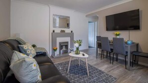 Ein Wohnzimmer mit Kamin, eine Essecke mit Fernseher und eine Couch mit Zierkissen.
