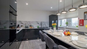 A modern kitchen with a marble backsplash, black cabinets, and a dining area with a long table set for four. - William Wallace View - 5 Bedroom House Near Castle (Stirling)