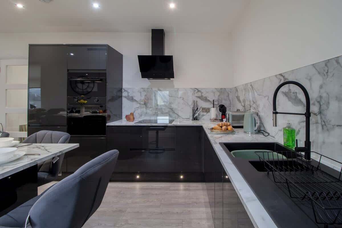 A modern kitchen with a marble backsplash, a black island, and a dining area with a table and chairs.