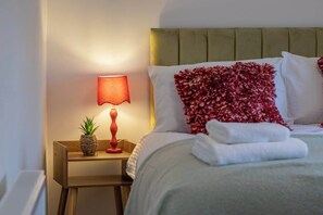 A neatly made bed with a green headboard, a red lamp on a wooden nightstand, and a pineapple decoration. - William Wallace View - 5 Bedroom House Near Castle (Stirling)