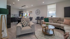 A modern living room with a sofa, armchair, coffee table, and a dining area in the background. - William Wallace View - 5 Bedroom House Near Castle (Stirling)