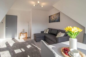 A modern living room with a grey sofa, a white vase with yellow flowers, and a small side table with a lamp. - Thistle View - Sleeps 4 by the Coast of Largs (Largs)