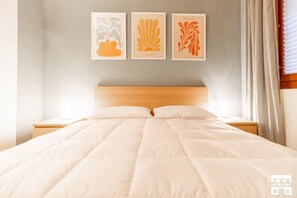 A neatly made bed with a wooden headboard, a bedside table, and three framed artworks on the wall. - GRABBIA 5 by Design Studio (Bellano)