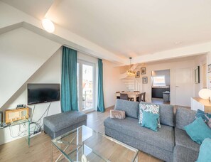 A modern living room with a sofa, glass coffee table, and a flat-screen TV. - 3-bedroom Sunny Apartment in Knokke (Knokke-Heist)
