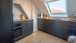 A modern kitchen with a skylight, built-in oven, and dark cabinetry. - 3-bedroom Sunny Apartment in Knokke (Knokke-Heist)