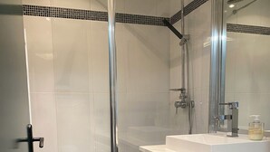Une salle de bain moderne dotée d’une douche à parois de verre, d’un lave-linge encastré et d’un lavabo avec un miroir au-dessus.