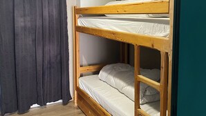 Un lit superposé avec une structure en bois, un matelas blanc et un rideau gris.