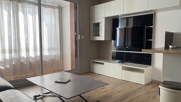 Un salon moderne doté d’une porte-fenêtre coulissante, d’un téléviseur à écran plat, d’un four à micro-ondes encastré et d’une petite table basse.