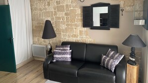 Un salon avec un mur en pierre, un canapé en cuir noir, deux lampes et un miroir.