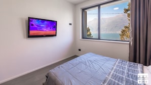 A bedroom with a bed, a TV on the wall, a window with a mountain view, and a curtain. - Enjoy a relaxing stay in this cozy apartment located just above the Bellano hill. The elevated position offers splendid views of Lake Como, perfect for unforgettable sunsets. The apartment includes a private parking space and all the amenities for a peac (Bellano)