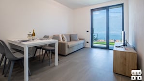 A modern living room with a dining table, sofa, and a view of the outdoors through a large sliding door. - Enjoy a relaxing stay in this cozy apartment located just above the Bellano hill. The elevated position offers splendid views of Lake Como, perfect for unforgettable sunsets. The apartment includes a private parking space and all the amenities for a peac (Bellano)