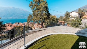 A residential property with a stone pathway leading to a grassy area, overlooking a lake and mountains. - Enjoy a relaxing stay in this cozy apartment located just above the Bellano hill. The elevated position offers splendid views of Lake Como, perfect for unforgettable sunsets. The apartment includes a private parking space and all the amenities for a peac (Bellano)