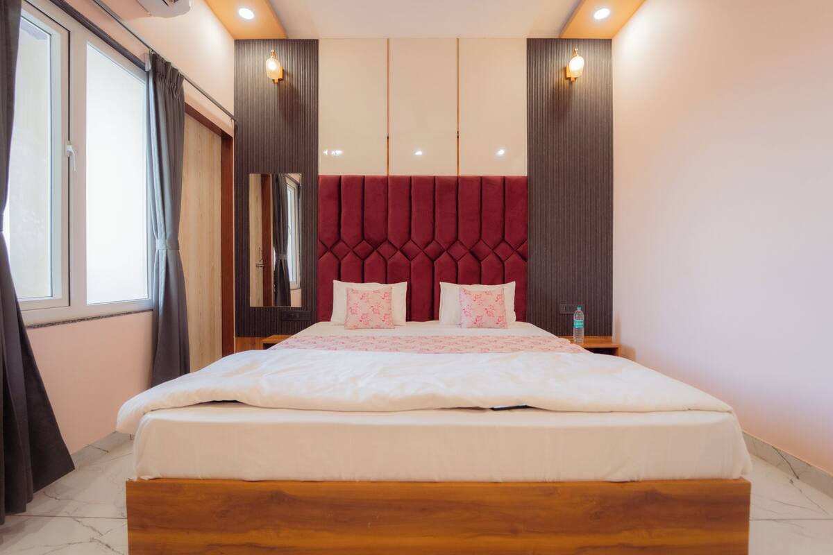 A hotel room with a large bed, a wooden headboard, a mirror, and a window with curtains.