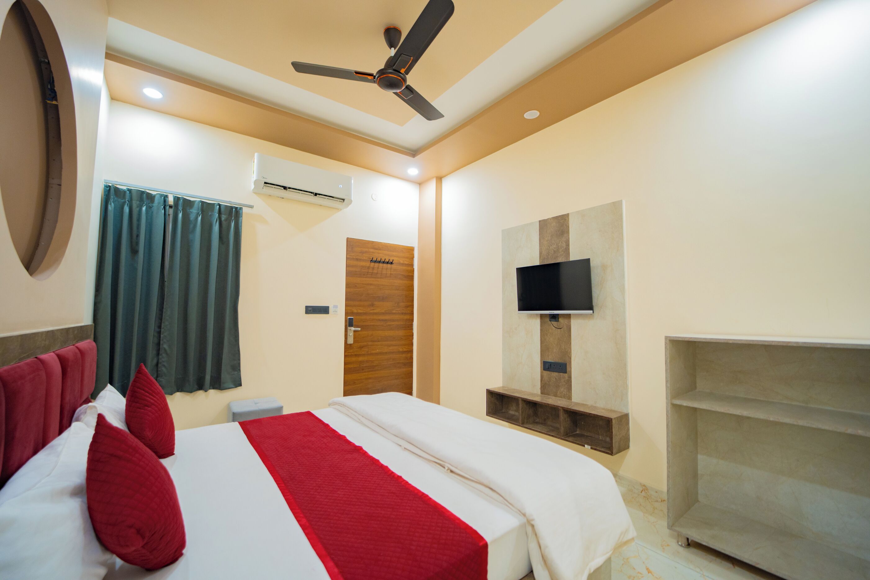 A hotel room with a bed, a ceiling fan, an air conditioning unit, a television, and a wooden door.